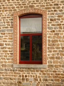 Fenêtre aluminium rouge sur mesure Solabaie installée sur une maison aux murs de pierres et de briques